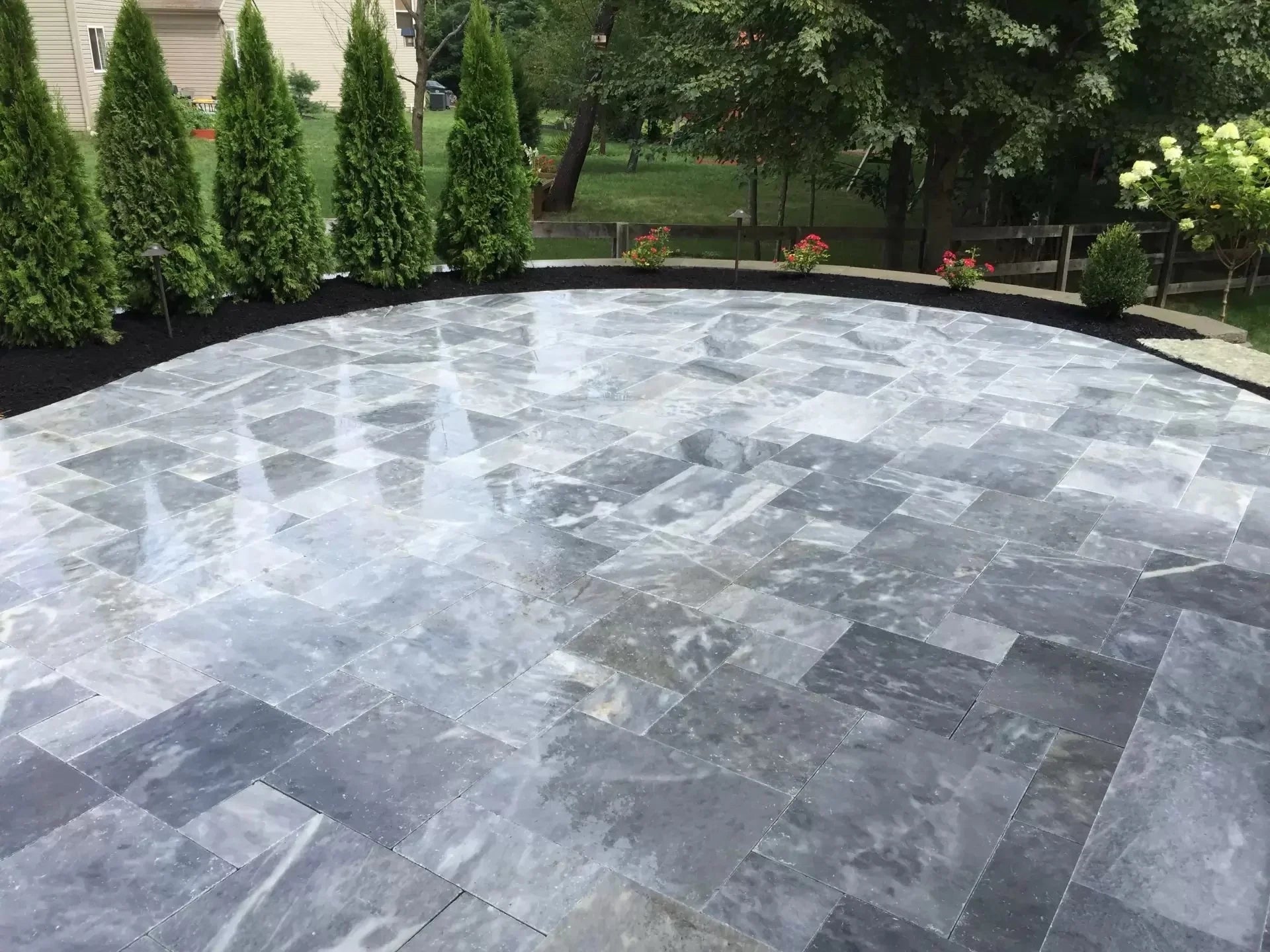 Round stone patio in a garden setting with greenery. Bluestone tumbled pavers pattern