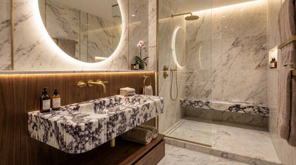 Luxurious bathroom with marble walls, a sink, and a shower.