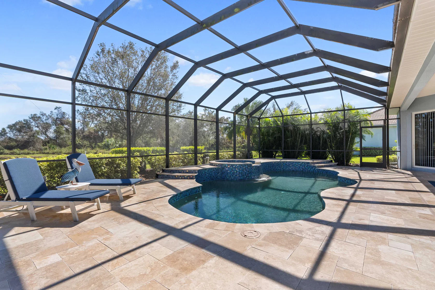 Pool area with lounge chairs and a screened-in enclosure under a clear blue sky. Denizli Beige Filled &amp; Tumbled Pavers (3 cm Thick)