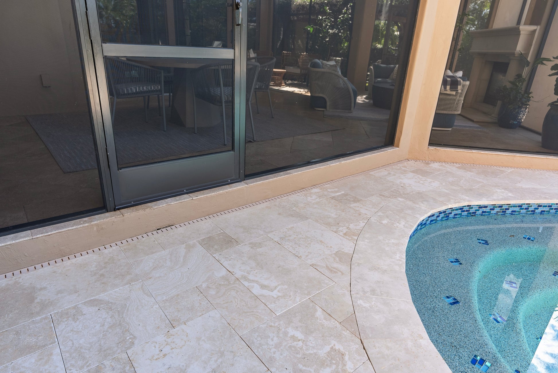 Outdoor patio area with a pool and sliding glass door. Ivory Moderno Travertine Filled and Tumbled Pavers