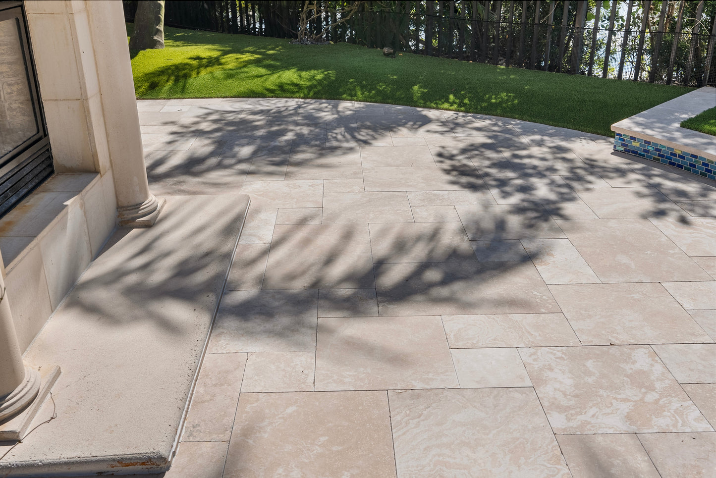 Outdoor patio with stone tiles and a view of grass and trees. Ivory Moderno Travertine Filled and Tumbled Pavers