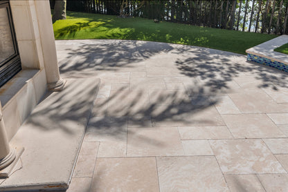 Outdoor patio with stone tiles and a view of grass and trees. Ivory Moderno Travertine Filled and Tumbled Pavers