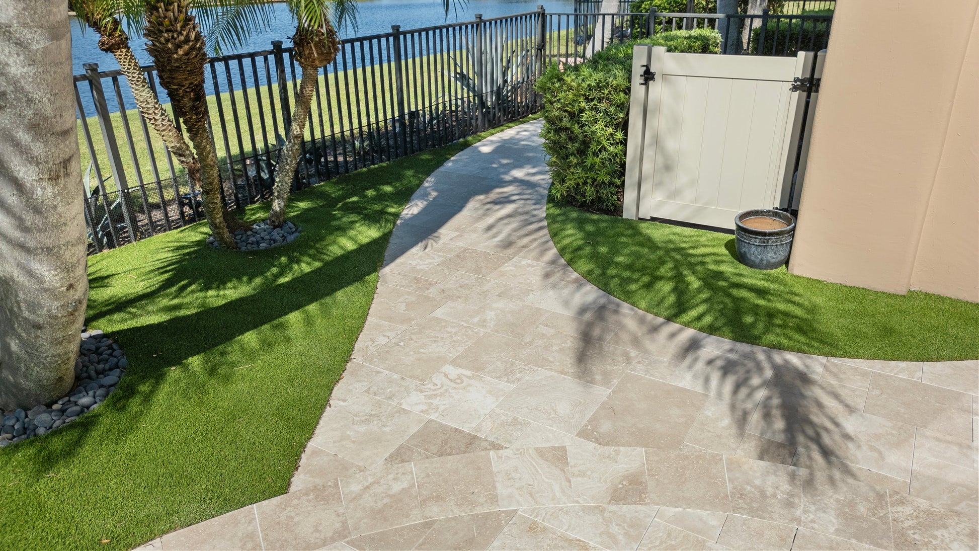 Paved patio area with grass and a fence in the background. Ivory Moderno Travertine Filled and Tumbled Pavers
