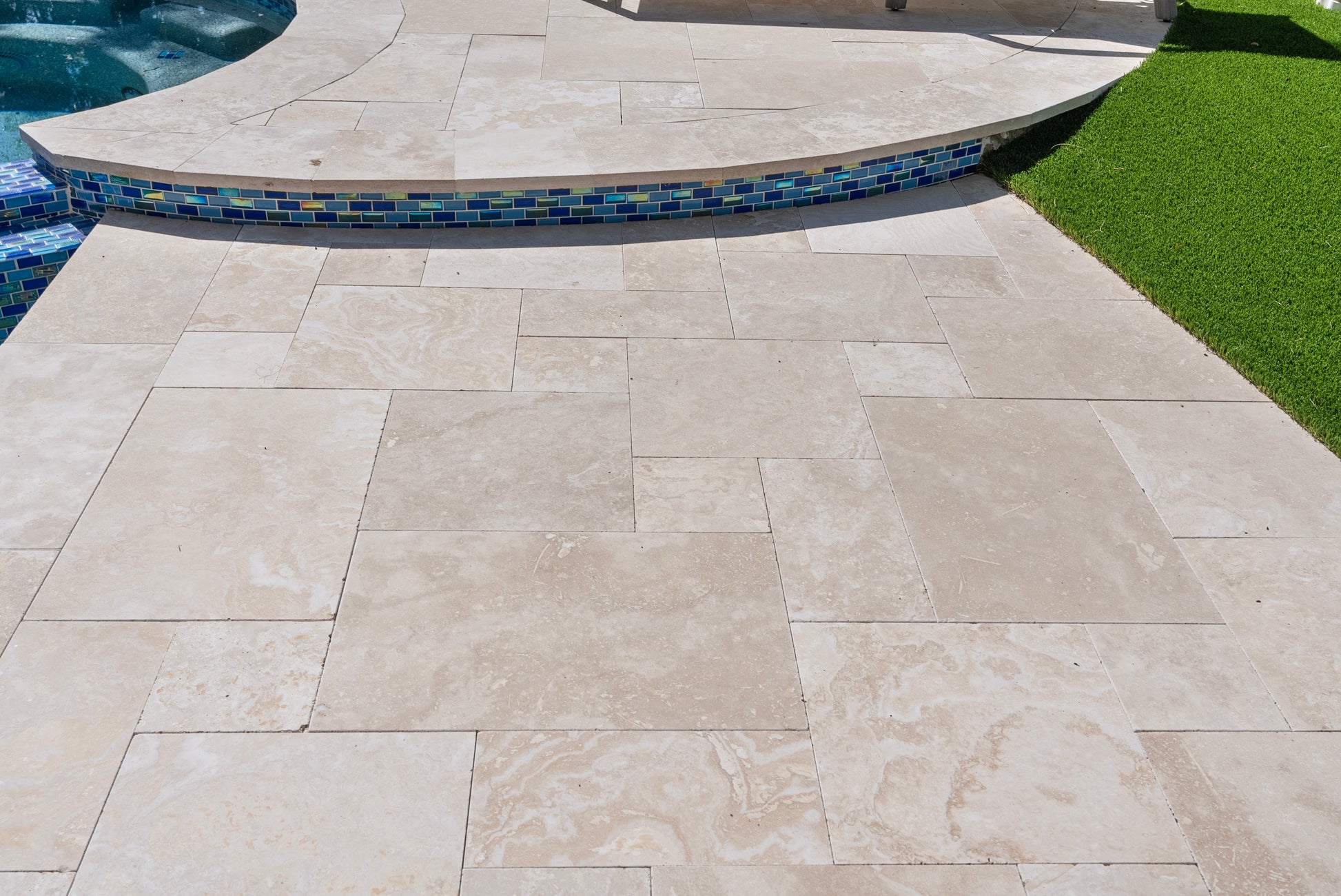 Beige stone tiles on a patio with a pool and grass in the background