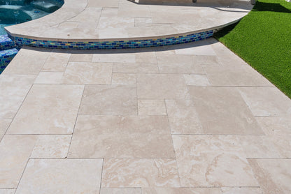 Beige stone tiles on a patio with a pool and grass in the background
