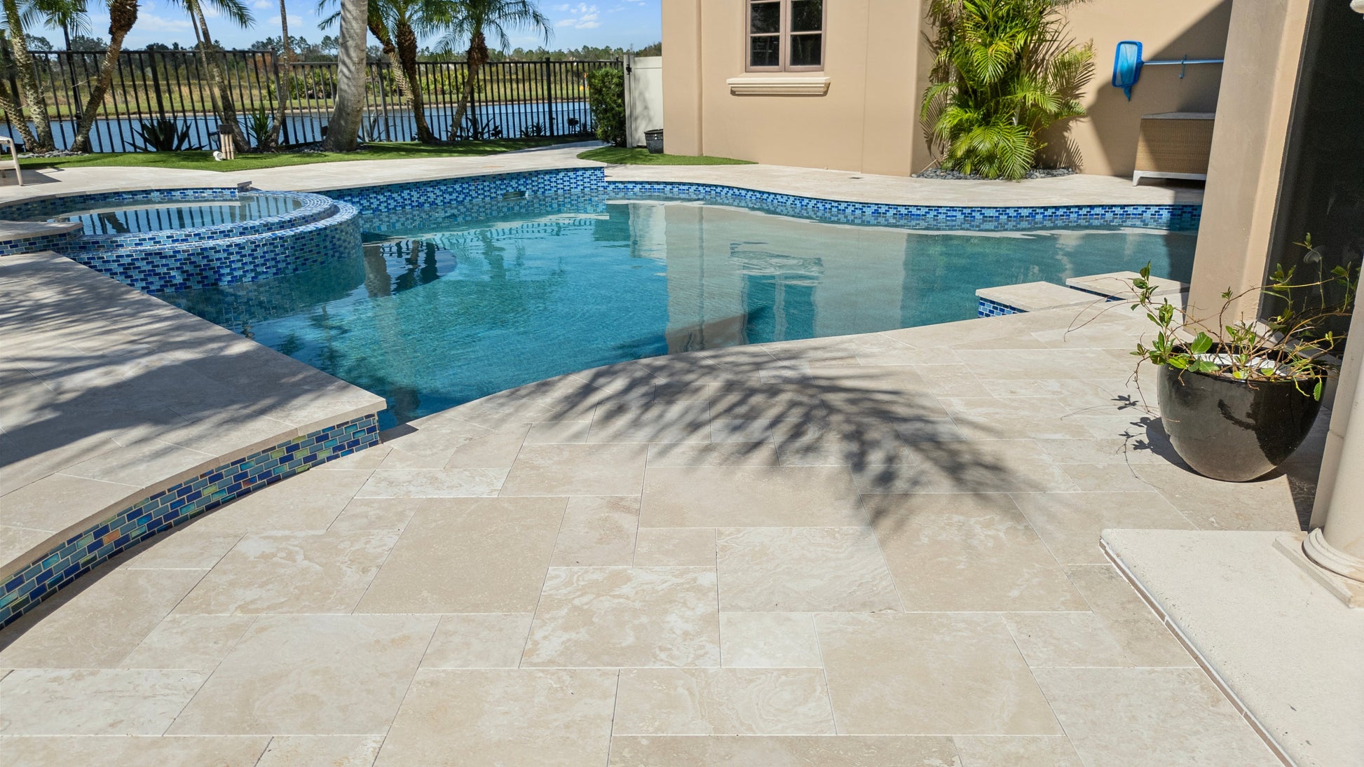 Pool area with tiled deck and palm tree shadow. Ivory Moderno Travertine Filled and Tumbled Pavers