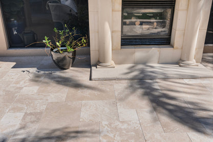 Paved patio area with a plant pot and architectural columns. Ivory Moderno Travertine Filled and Tumbled Pavers