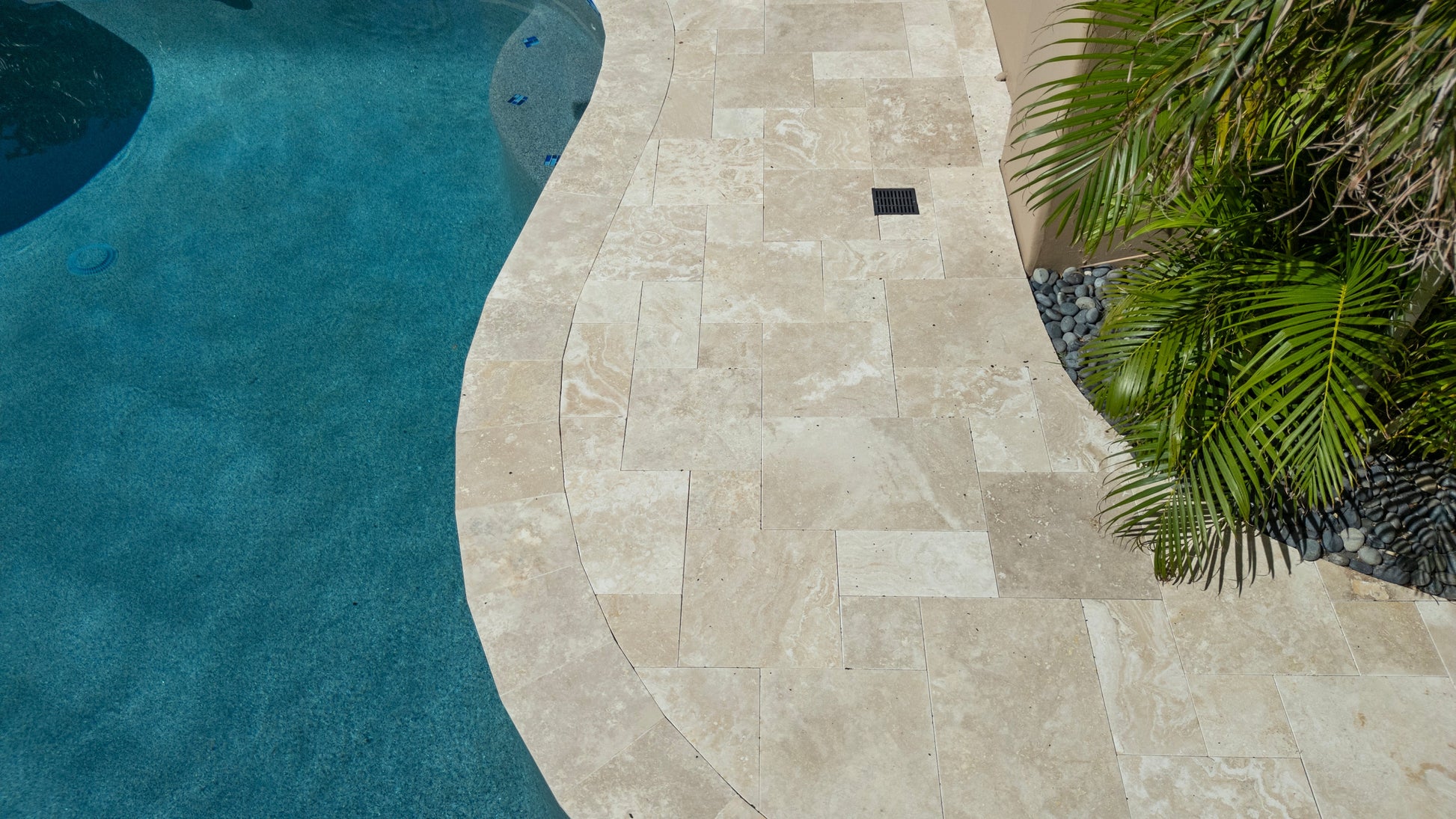 Beige stone pathway leading to a pool with greenery on the side. Ivory Moderno Travertine Filled and Tumbled Pavers