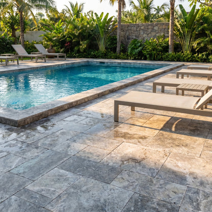 Pool area with lounge chairs and tropical plants. Silver Travertine Tumbled Pavers