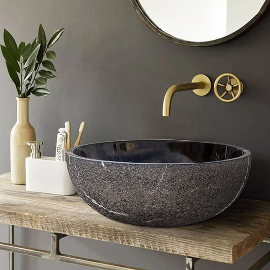 Toros Black Marble Above-Vanity Bathroom Vessel Sink Rough Exterior (D)16" (H)6" installed above wooden vanity with metal frames gold color faucet and toothbrushes and toothpaste bathroom set with beige color vase and green flowers