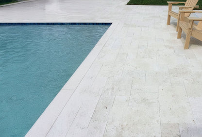 Poolside area with a pool and a wooden chair on a light-colored deck. Shell Stone White Tumbled Limestone Pavers