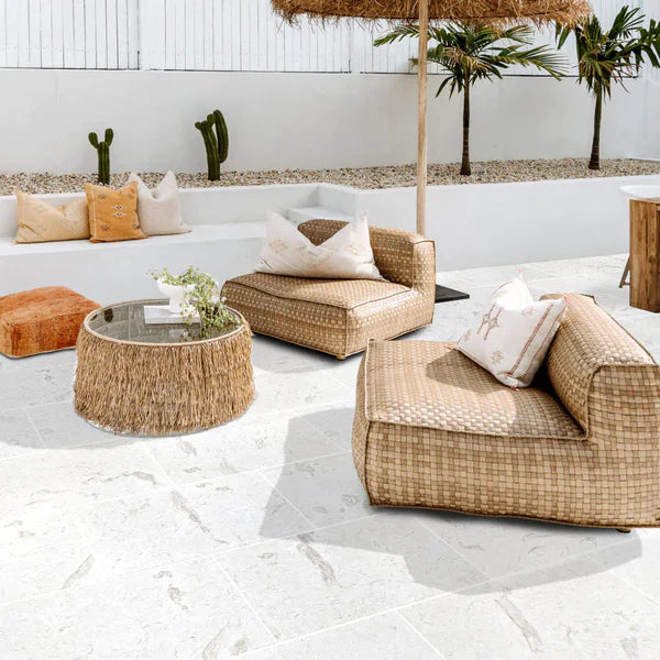 Outdoor patio with wicker furniture, cushions, and a umbrella on a white tiled floor. Shell Stone White Tumbled Limestone Pavers